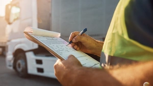 Close up of cargo dispatcher writing on clipboard on truck parking lot.